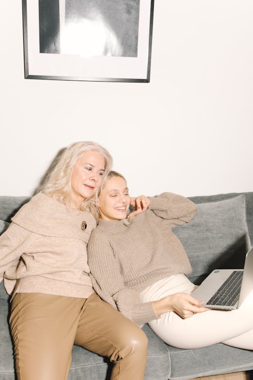  Mother And Daughter Sitting On A Gray Couch Watching Using A Laptop