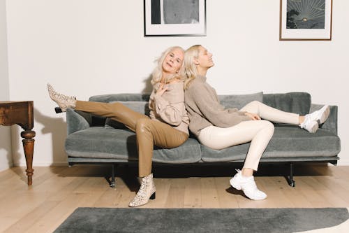 Free Mother And Daughter Sitting Back To Back on Gray Couch Stock Photo