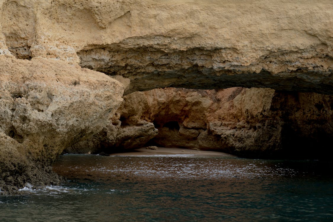 Brown Rock Formation With Cave Beside Body of Water · Free Stock Photo