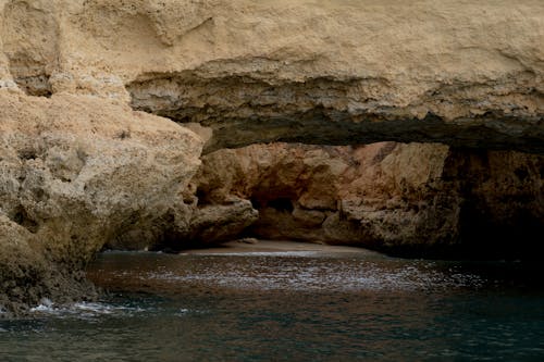 Free Brown Rock Formation With Cave Beside Body of Water Stock Photo