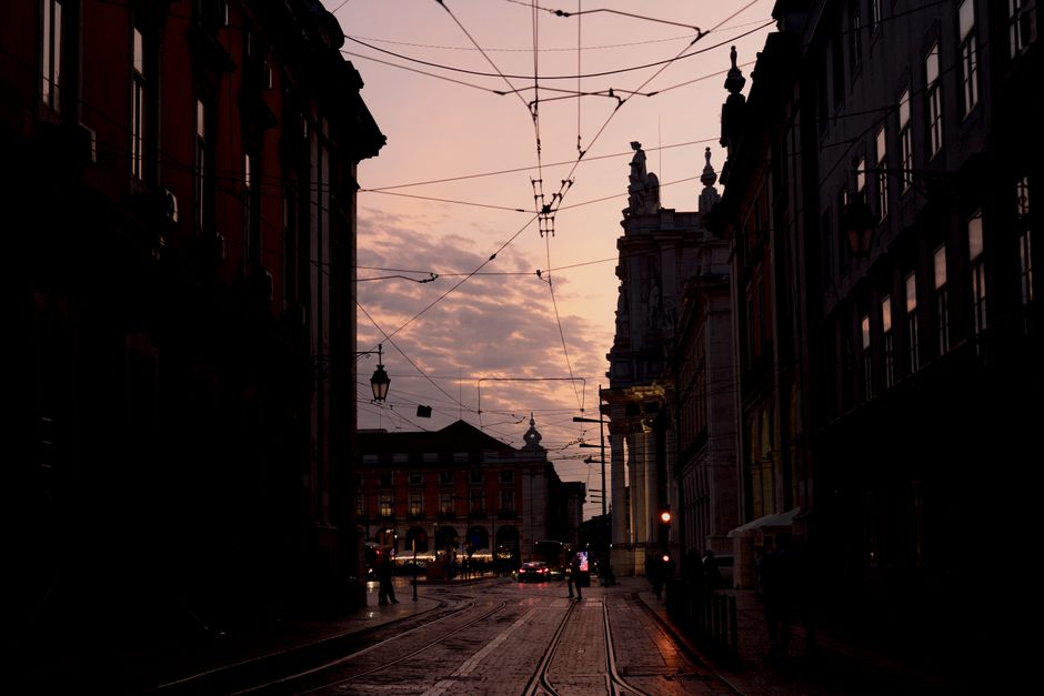 Urban street view of Lisbon with tram lines silhouetted against twilight sky.