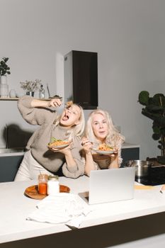 Two joyful women enjoying a cooking session together in the kitchen, embracing family time and Italian cuisine.