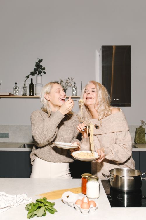 Free Mother and daughter sharing a joyful moment cooking pasta together in a modern kitchen. Stock Photo