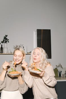 A joyful mother and daughter enjoying spaghetti together in a cozy kitchen.