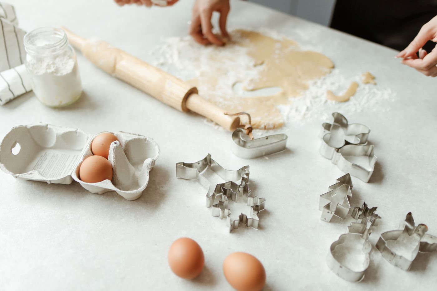 Rolling pin, flour, eggs, dough and baking cutters arranged on a kitchen counter