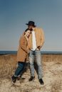 Man in Brown Jacket and Blue Denim Jeans Standing on Brown Grass Field