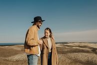 Man in Brown Coat and Blue Denim Jeans Standing on Brown Sand