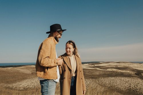 Free A cheerful couple holding hands and smiling in a beautiful outdoor setting with rolling dunes. Stock Photo