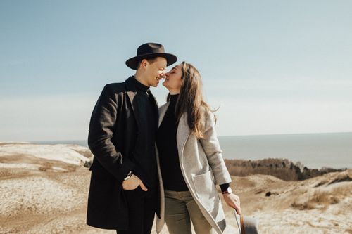Free Happy couple in fashionable attire embracing outdoors with a scenic backdrop in the distance, conveying warmth and style. Stock Photo
