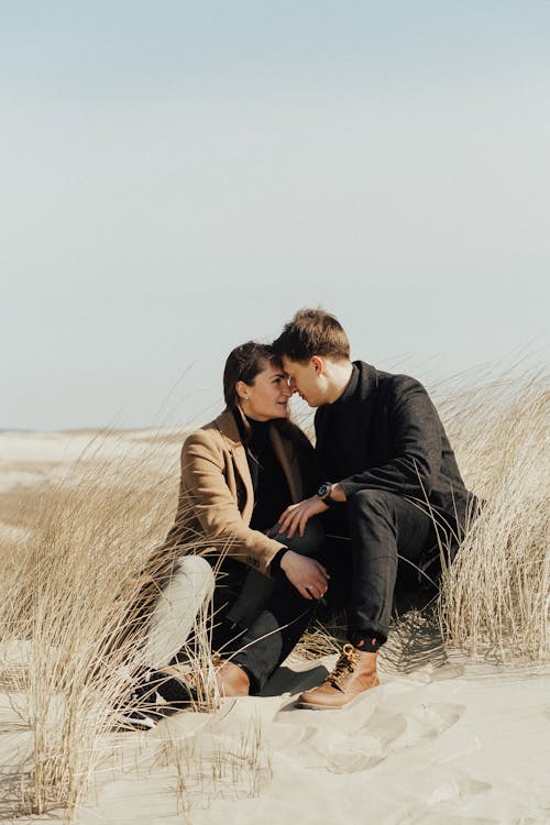 Free A Romantic Couple Sitting on the Sand while Looking at Each Other Stock Photo