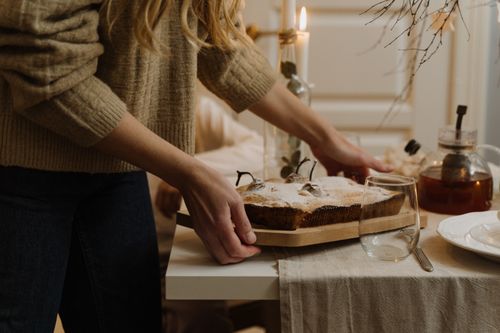 Free A warm, inviting scene of a person placing a homemade cake on a table set for dessert, surrounded by soft candlelight. Stock Photo