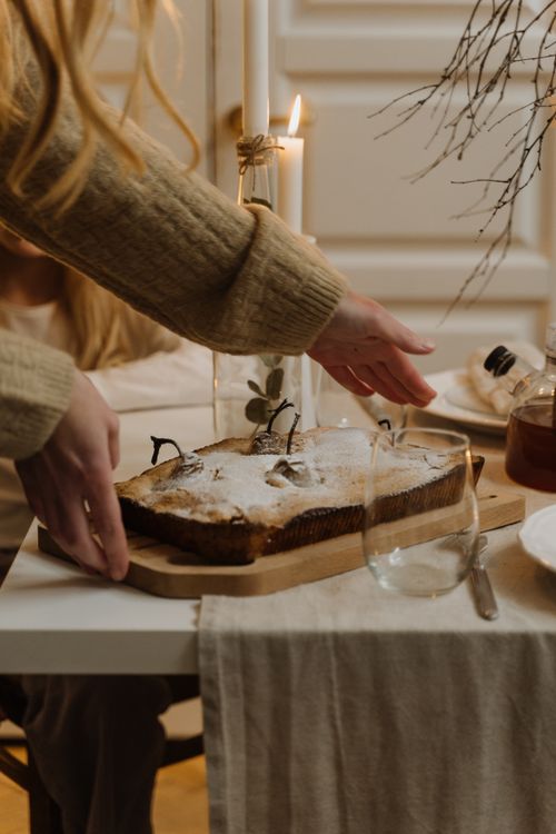 Free A cozy indoor setting featuring a homemade cake being placed on a table surrounded by warm lighting and decorations. Stock Photo