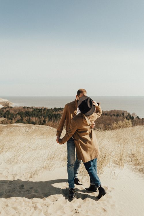 Free A couple embracing on dunes with a scenic coastal backdrop, capturing togetherness and love. Stock Photo