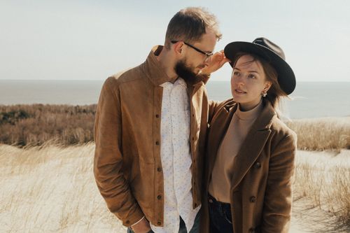 Free A fashionable couple stands on the beach dunes in stylish attire, enjoying a sunny day. Stock Photo