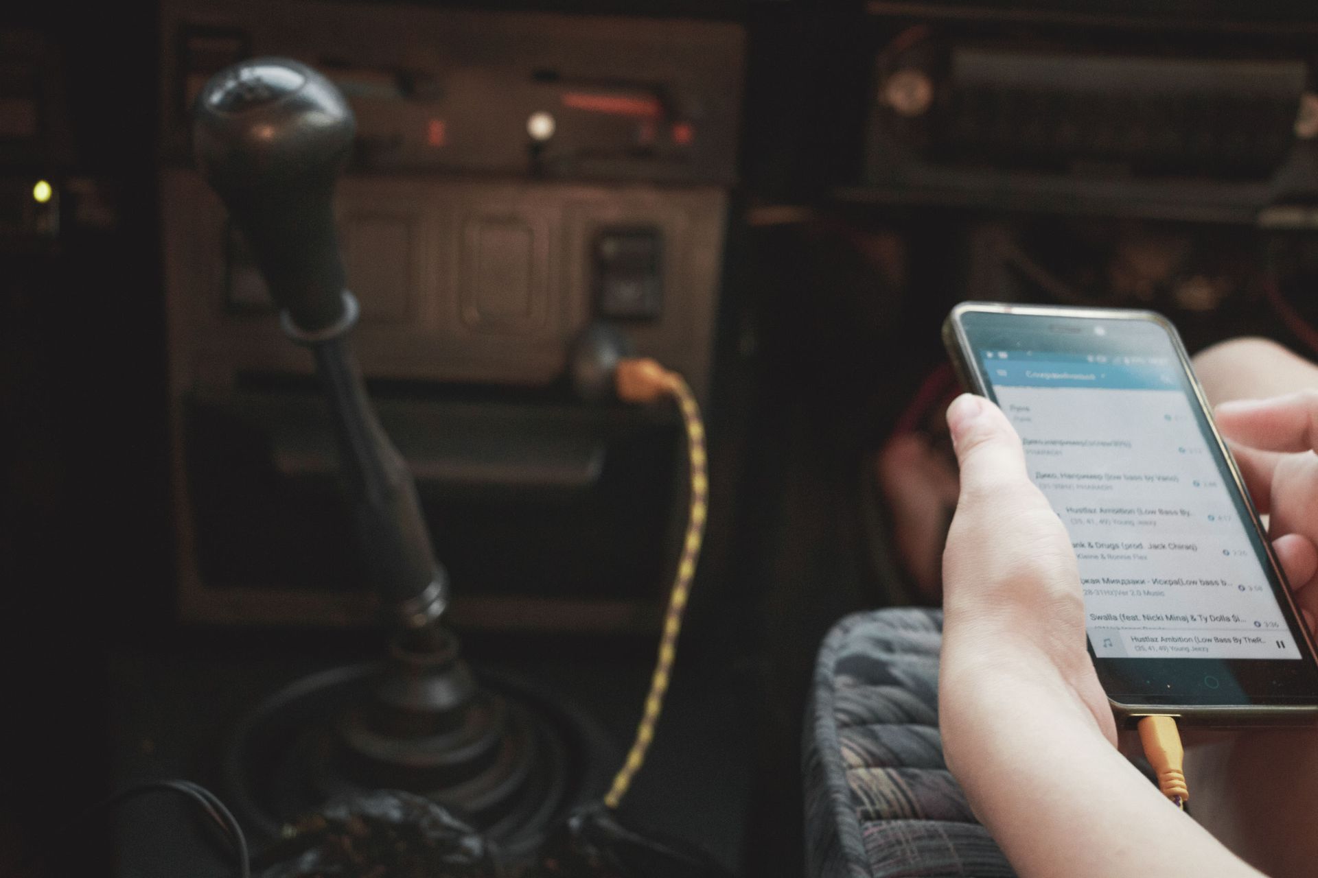Person using smartphone in vintage car interior, connected through cable.