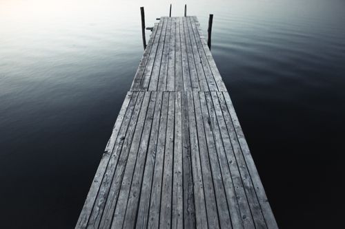 Free From above of narrow wooden boardwalk with pillars placed on pier near tranquil clear water in nature in coastal terrain Stock Photo