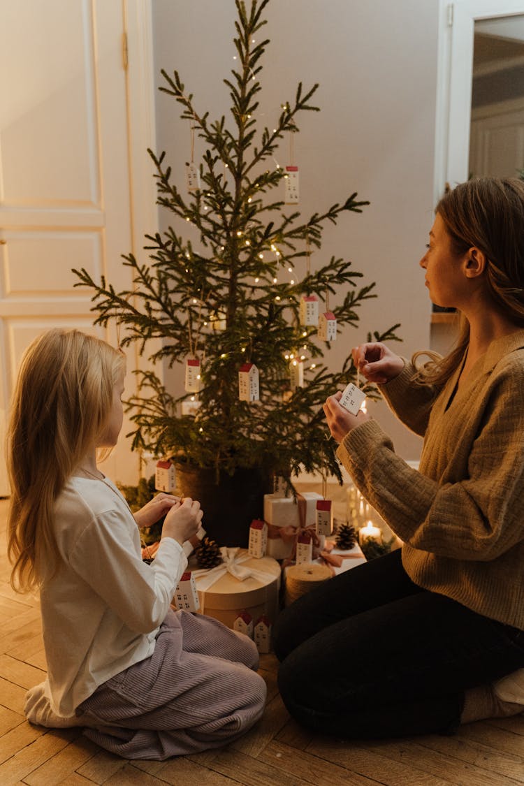 Woman And A Girl Decorating The Christmas Tree Together 