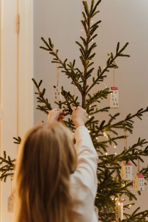 Free A blonde child decorates a minimalist Christmas tree with handmade ornaments indoors. Stock Photo