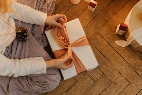 Free A woman wraps a beautifully decorated gift on a warm wooden floor, evoking a cozy Christmas atmosphere. Stock Photo