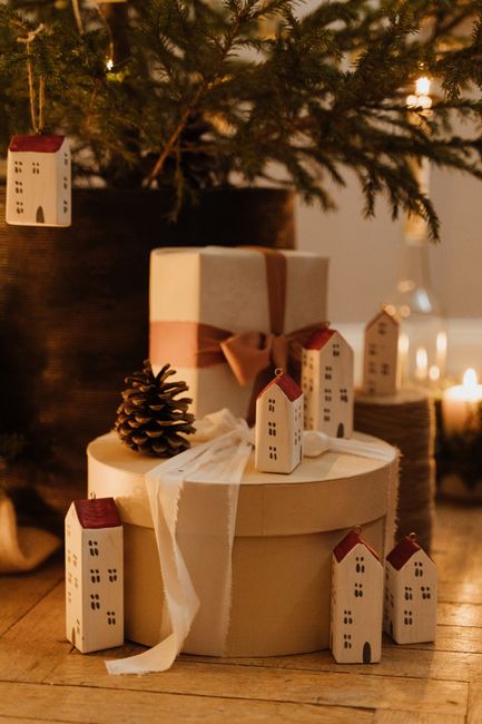Warm and festive Christmas gifts under a tree with charming mini house ornaments.
