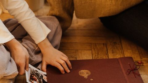 A mother and child sitting on a wooden floor organizing a photo album, creating family memories together.
