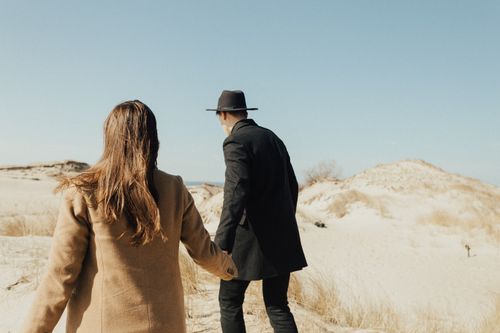 Free A couple walks hand in hand through a serene desert. Captivating back view under the clear sky. Stock Photo