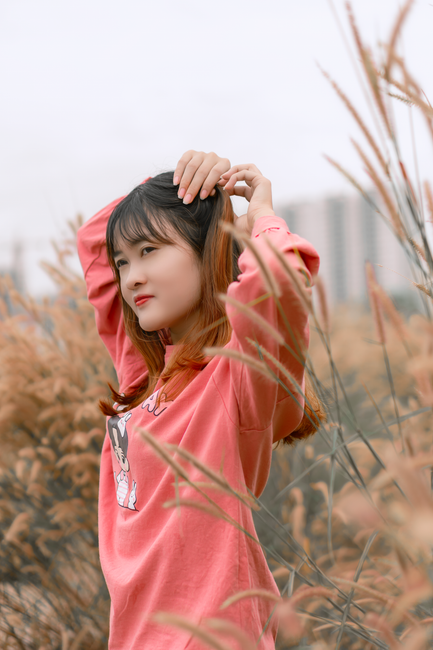 A young woman adjusts her hair outdoors surrounded by tall grass.