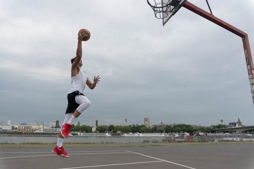 A man performs a high-flying basketball dunk on an outdoor court in Cologne, Germany.