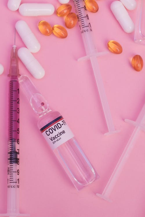 Top view arrangement of coronavirus vaccine placed on pink table near syringes and pills in modern hospital