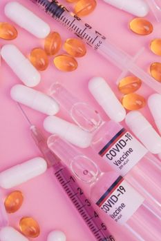 Top view ampoules of COVID 19 vaccine with syringes filled with remedy placed on pink surface near scattered pills and capsules