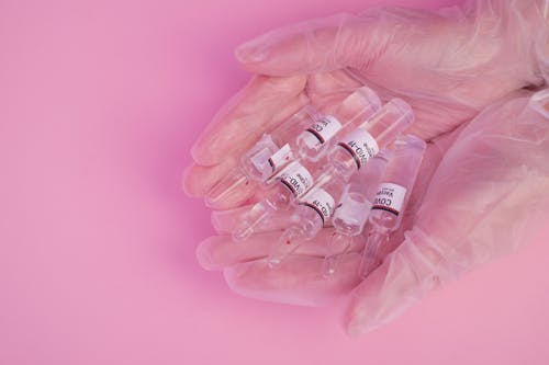Free Top view of crop faceless female doctor in latex gloves demonstrating heap of ampoules with COVID vaccine against pink background Stock Photo
