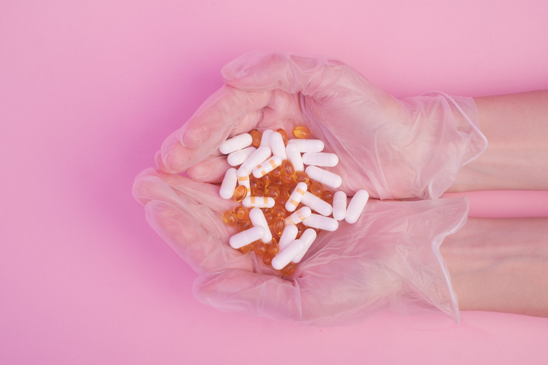 mebendazole for pre-cancerous polyps — From above crop anonymous female in sterile medical gloves with handful of various medicine capsules against pink background