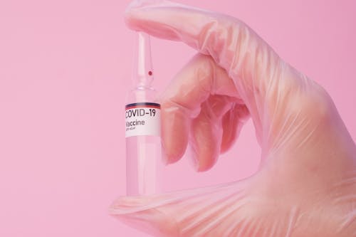 Unrecognizable scientist showing coronavirus vaccine ampoule against pink background