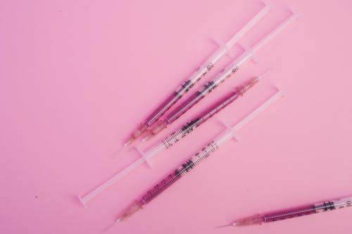 From above of syringes with needles filled with purple substance placed on pink background