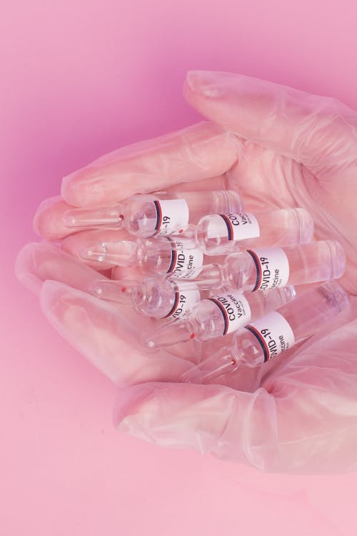 Free Crop woman demonstrating vials with COVID vaccine in pink studio Stock Photo