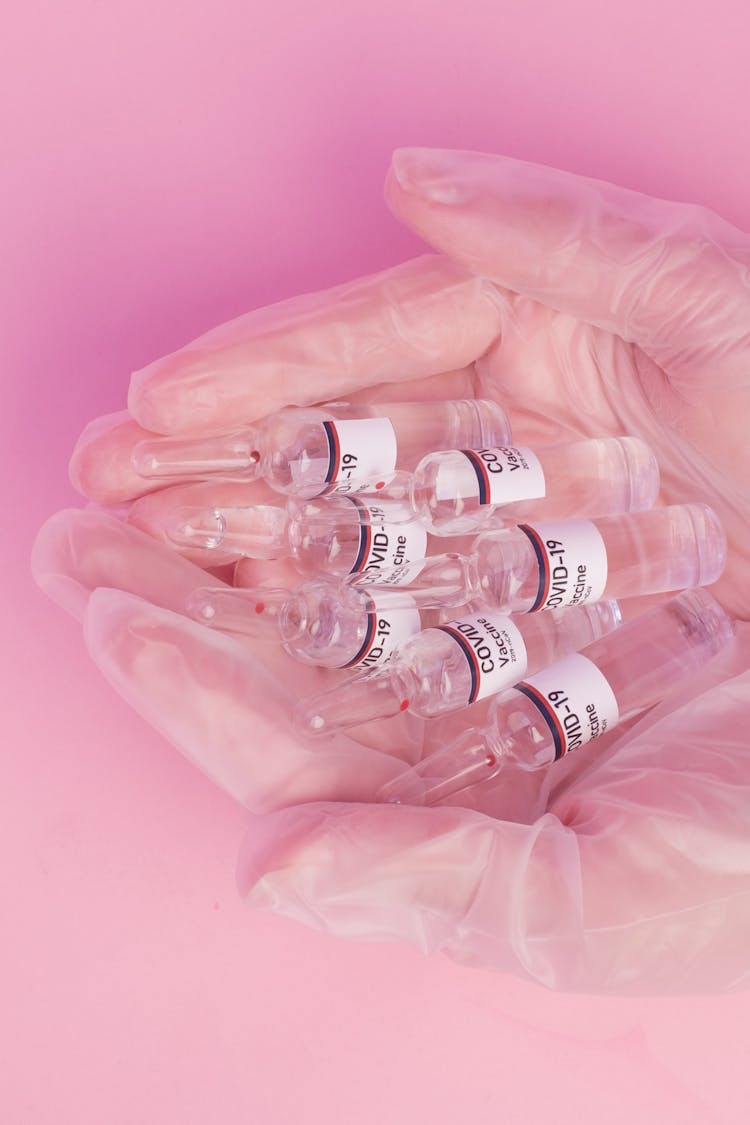 Crop Woman Demonstrating Vials With COVID Vaccine In Pink Studio