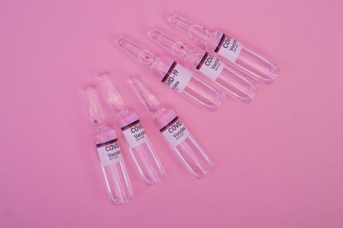 Top view set of sealed glass ampoules with COVID 19 vaccine arranged on pink surface