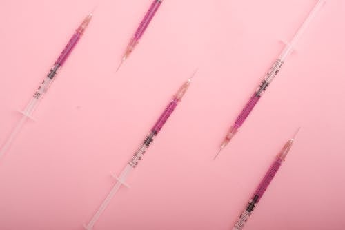 Top view set of syringes with purple colored liquid medicine arranged on pink background as background