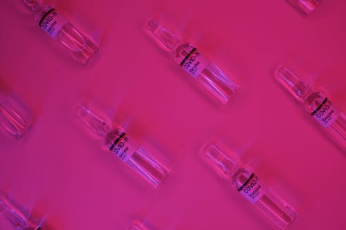 Top view of set of glass ampoules with COVID 19 vaccine arranged on bright pink surface under neon illumination