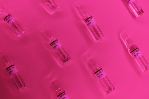 Free Layout of transparent glass vials of COVID 19 vaccine placed on pink table in laboratory Stock Photo