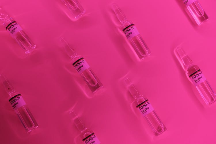 Ampules With COVID Drug Arranged On Pink Background In Bright Light