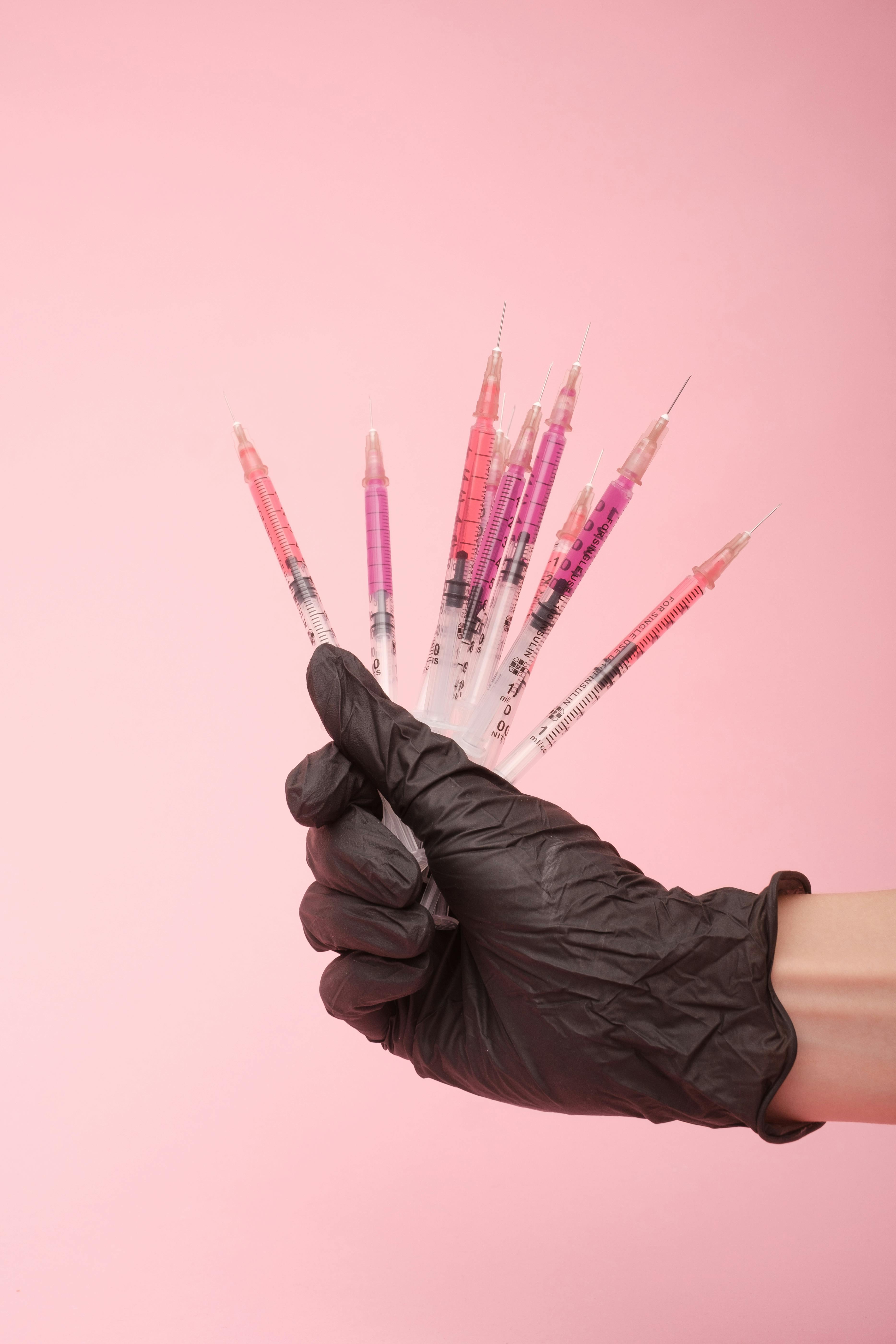 faceless doctor showing colorful syringes in pink studio