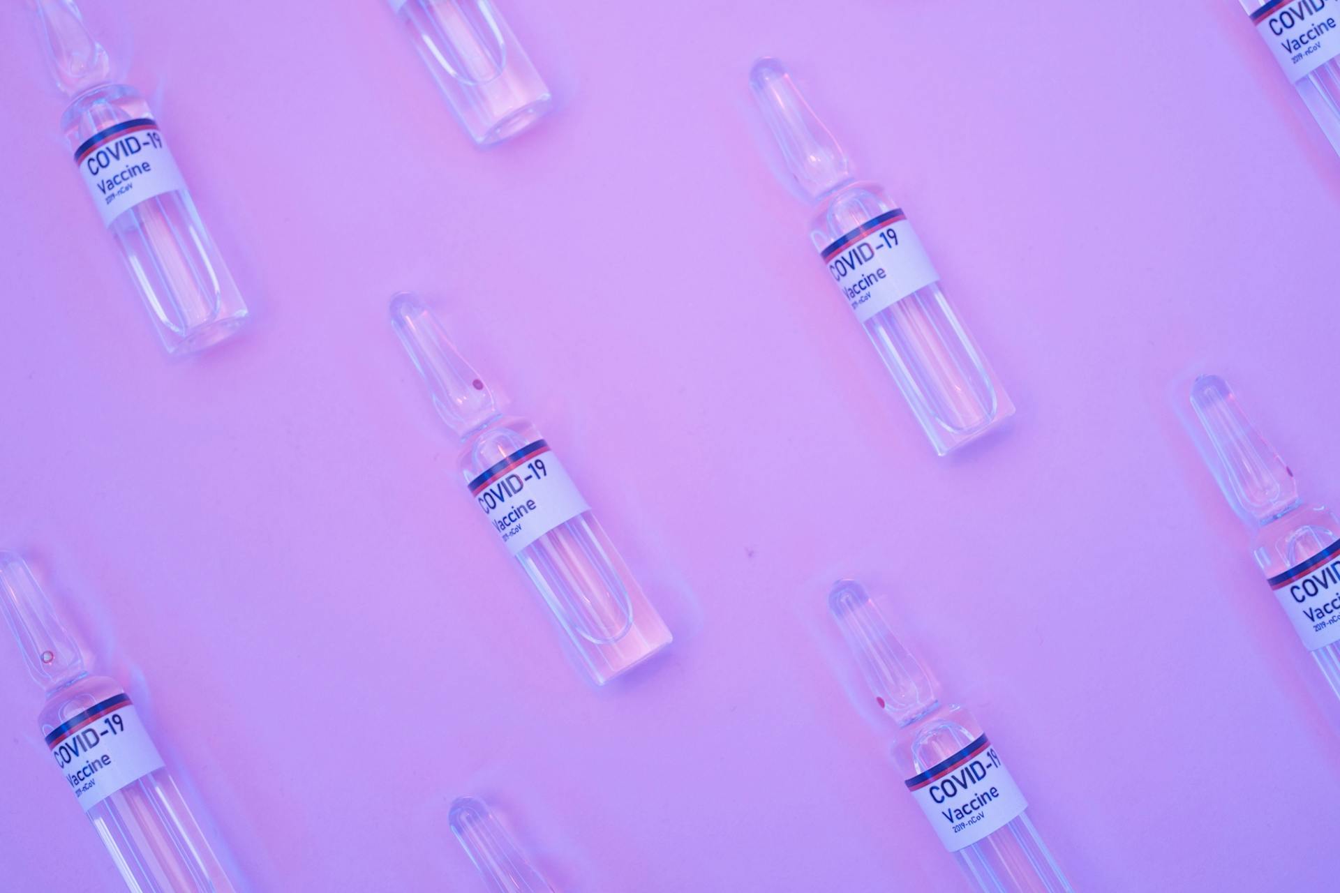 Background of similar ampoules with COVID 19 vaccine placed on table under neon purple light