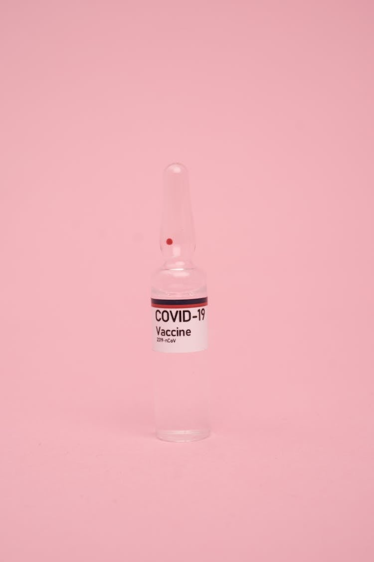 Medicine Vial With COVID 19 Vaccine Against Pink Background