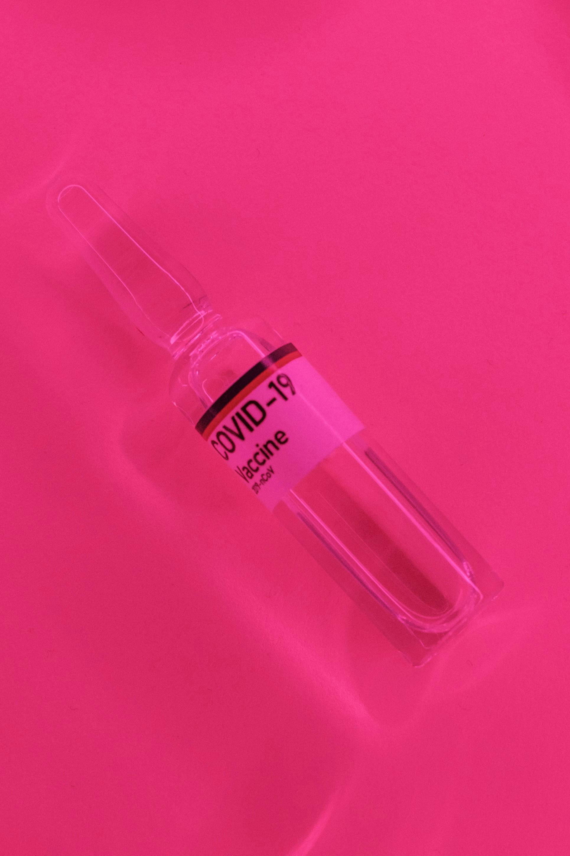 coronavirus vaccine in glass vial laced on vivid pink surface