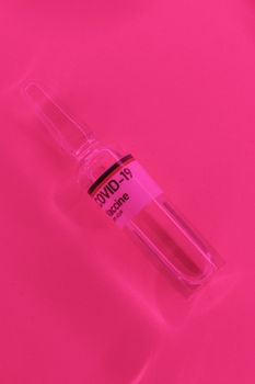 Top view glass ampoule with transparent liquid vaccine for COVID 19 placed on bright pink background