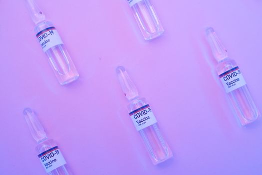 Top view of COVID-19 vaccine ampoules on a purple background for scientific research.