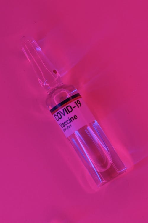 High angle of glass sealed vial containing coronavirus vaccine placed on vivid pink background