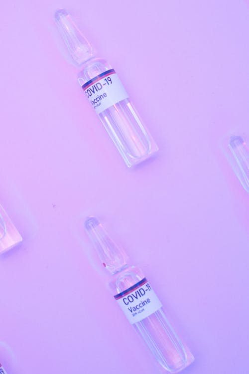 From above small glass vials with vaccine against COVID 19 arranged on purple background
