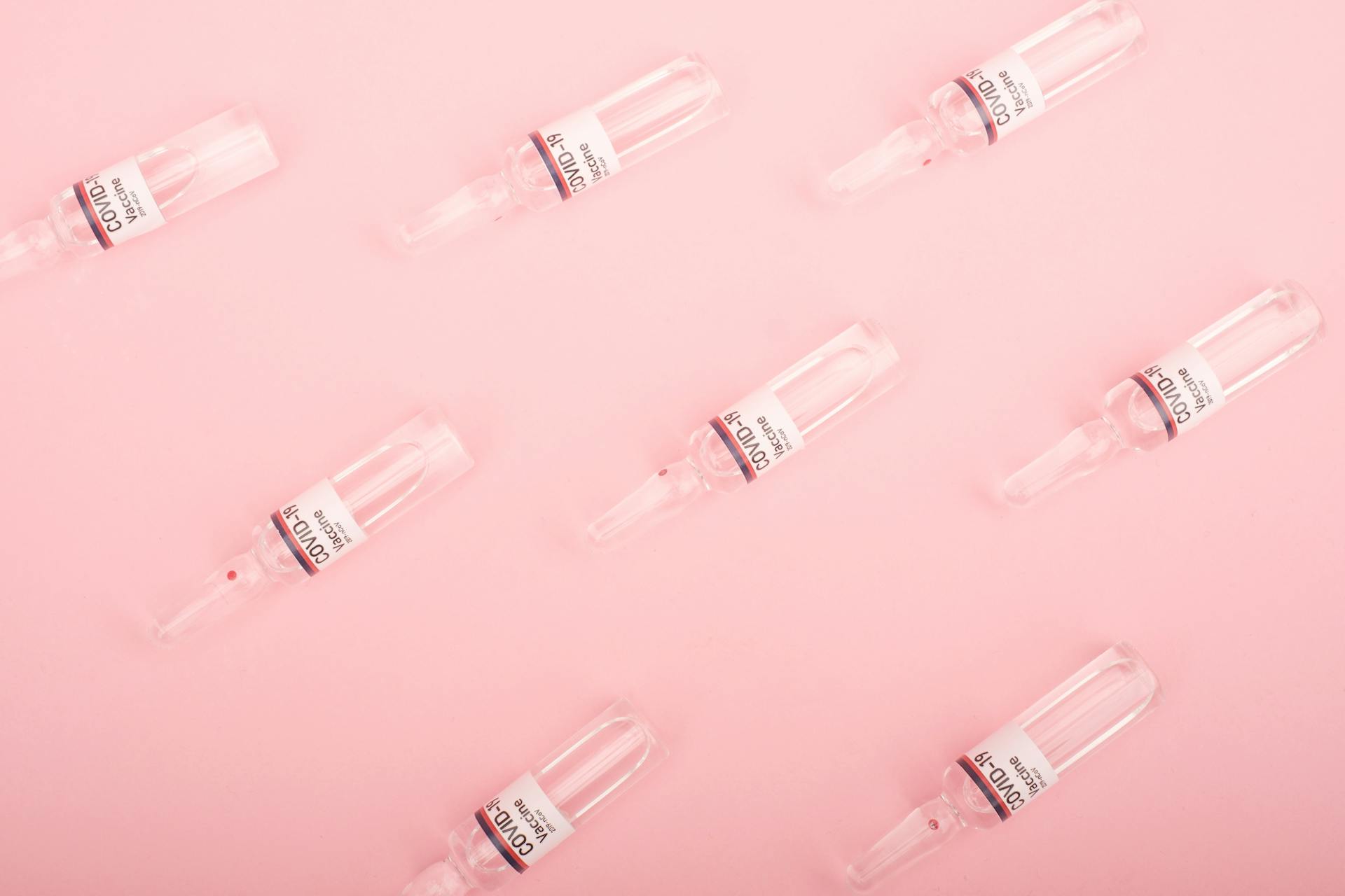 Collection of coronavirus vaccine vials placed on pink desk